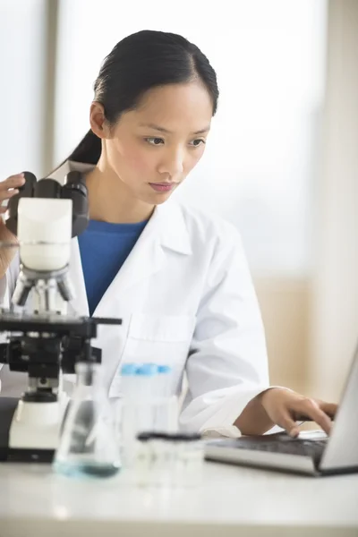 Arzt benutzt Laptop mit Mikroskop am Schreibtisch — Stockfoto