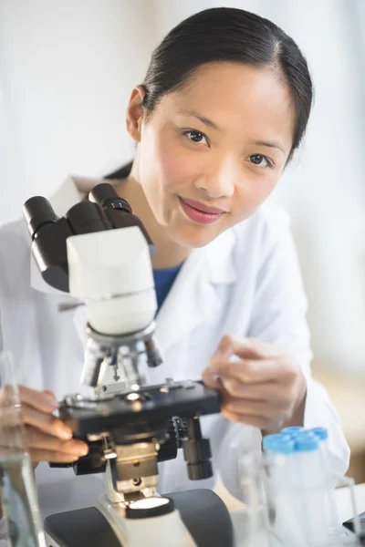 Cientista feminina sorrindo ao usar microscópio — Fotografia de Stock