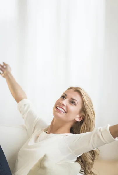 Mujer feliz con los brazos levantados relajante en el sofá —  Fotos de Stock