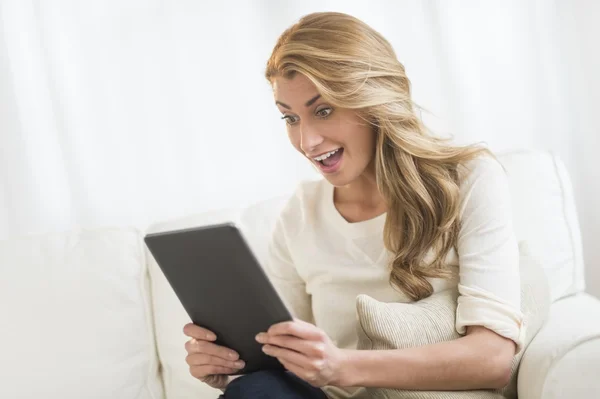 Женщина смотрит на цифровой планшет, сидя на диване — стоковое фото
