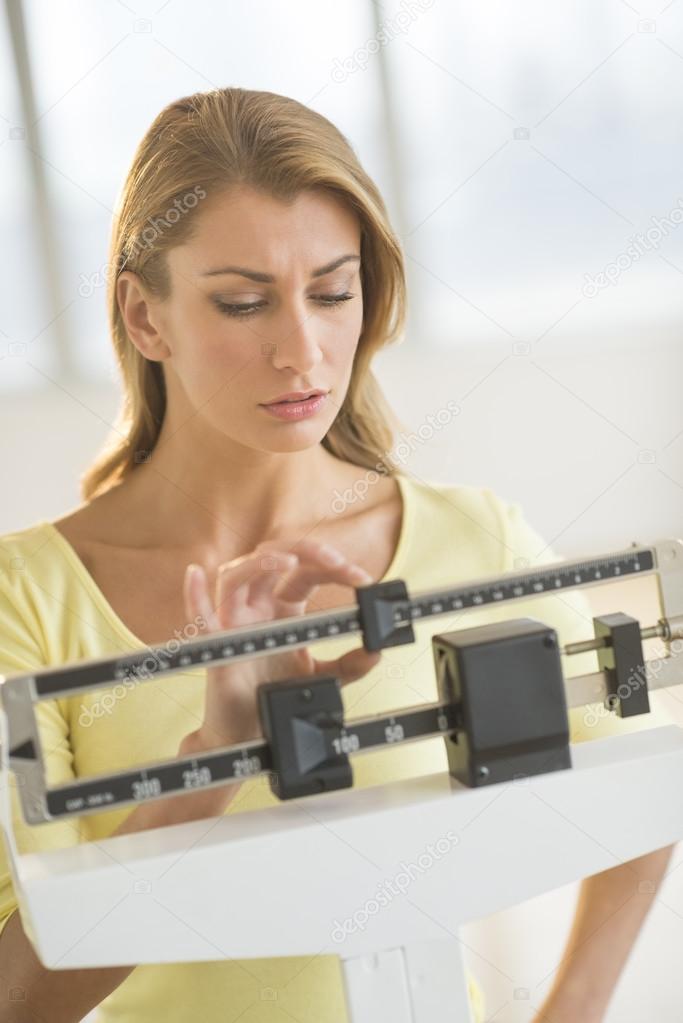 Woman Adjusting Weight Scale At Health Club