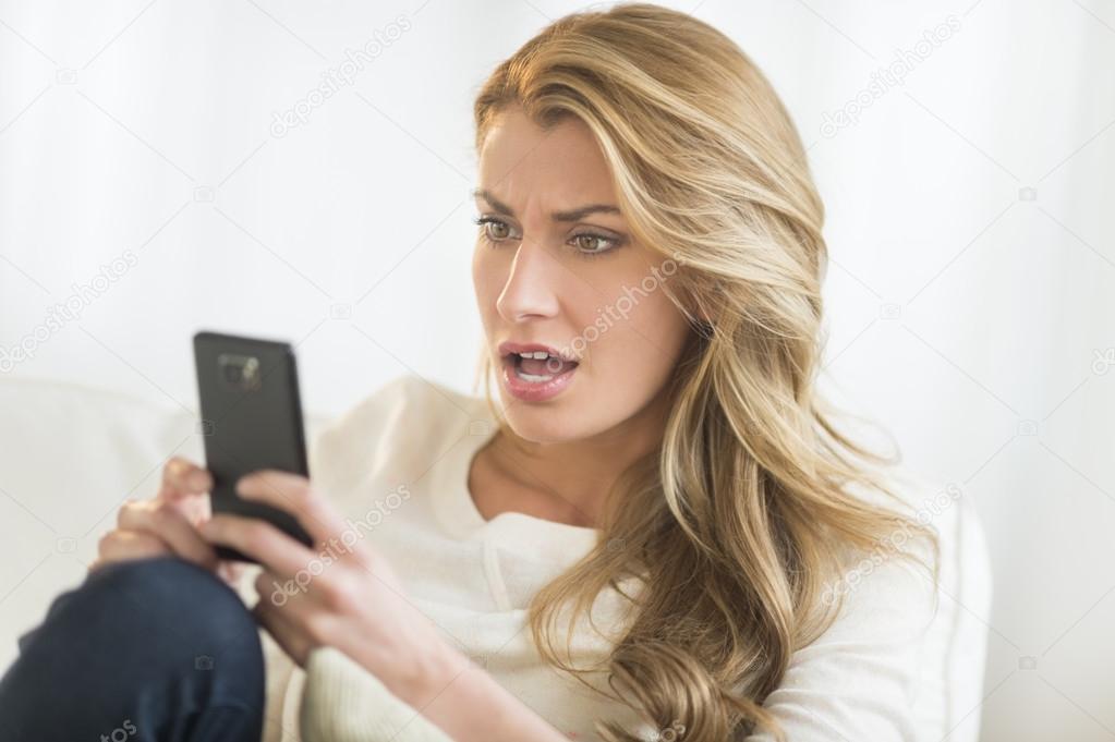 Amazed Woman Looking At Mobile Phone On Sofa