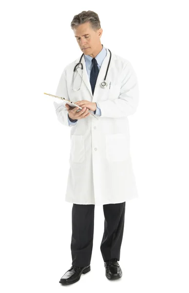 Male Doctor Looking At Clipboard Against White Background — Stock Photo, Image