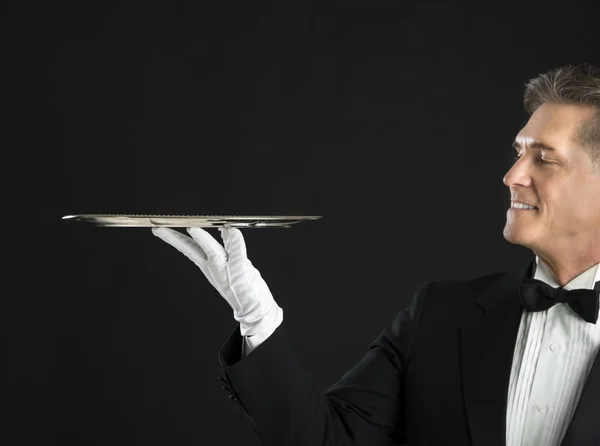 Camarero maduro sonriendo mientras mira bandeja de servicio —  Fotos de Stock