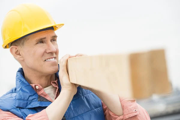 Trabajador mirando hacia otro lado mientras lleva una plancha de madera —  Fotos de Stock