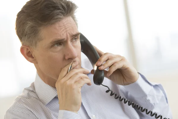 Homme d'affaires réfléchi utilisant le téléphone fixe dans le bureau — Photo