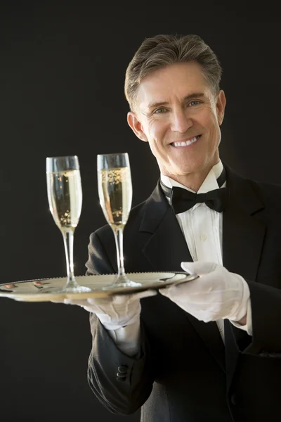 Garçom feliz segurando bandeja de serviço com flautas de champanhe — Fotografia de Stock