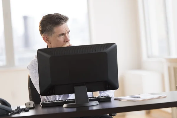 Pensativo hombre de negocios mirando hacia otro lado mientras está sentado en el escritorio en off — Foto de Stock