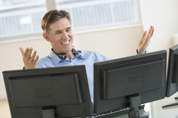 Happy Trader Gesturing While Using Multiple Screens At Desk