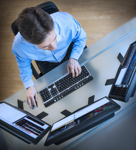 Trader Analyzing Data On Multiple Screens At Desk