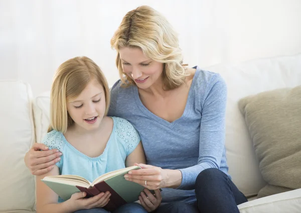 Mãe e filha lendo livro juntos no sofá — Fotografia de Stock