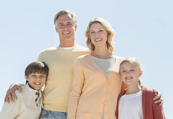 Gelukkige familie van vier staande tegen duidelijke blauwe hemel — Stockfoto