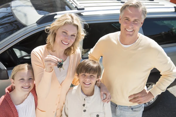 Femme montrant des clés tout en se tenant debout avec la famille contre la voiture — Photo