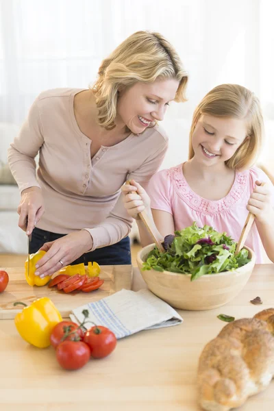 Mädchen unterstützt Mutter bei der Zubereitung von Salat an der Theke — Stockfoto