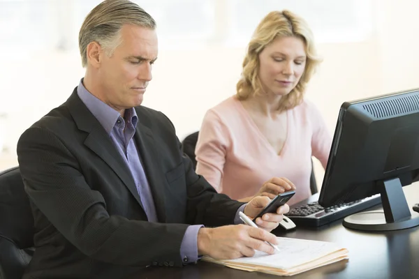 Empresário usando telefone celular enquanto colega de trabalho na mesa — Fotografia de Stock