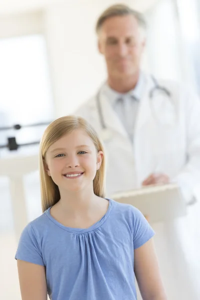 Menina sorrindo com o médico em pé no fundo na clínica — Fotografia de Stock