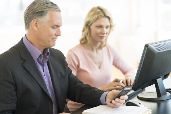 Zakenman die mobiele telefoon terwijl collega met behulp van computer — Stockfoto