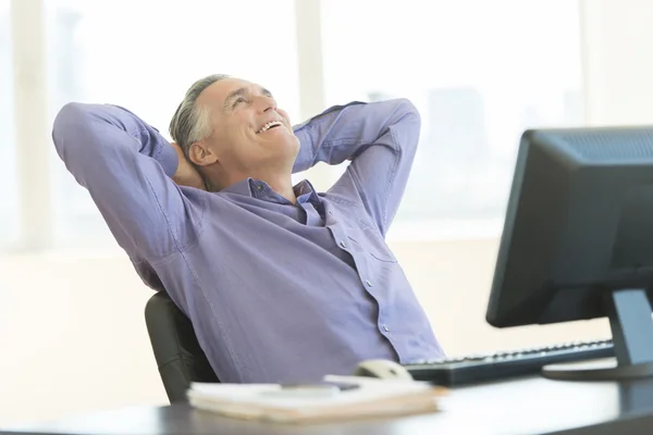 Glad affärsman med händerna bakom huvudet ser i office — Stockfoto