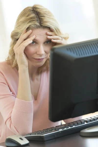 Geschäftsfrau mit Kopf in den Händen blickt auf Computermonitor — Stockfoto