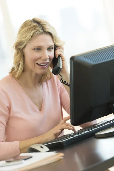 Affärskvinna tittar på datorn svara på telefon i o — Stockfoto