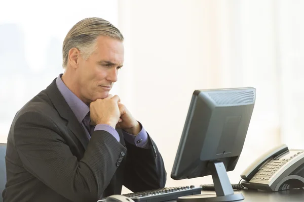 Empresário sério olhando para o PC desktop no escritório — Fotografia de Stock