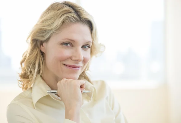 Empresaria con la mano en la barbilla sonriendo en la oficina — Foto de Stock