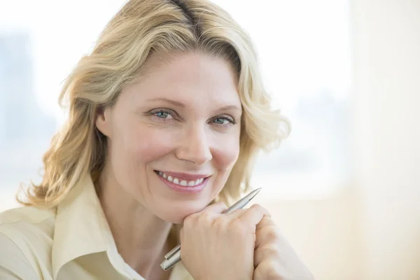 Kobieta z ręki na brodzie uśmiechający się w biurze — Zdjęcie stockowe