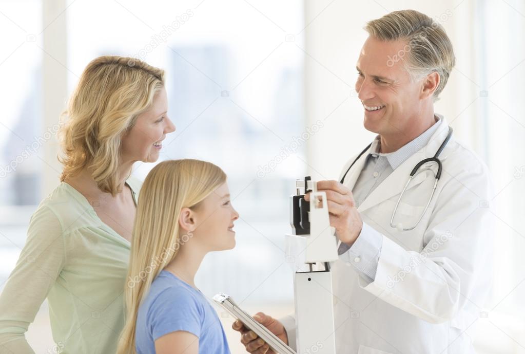 Doctor Examining Girl's Weight While Looking At Woman In Clinic