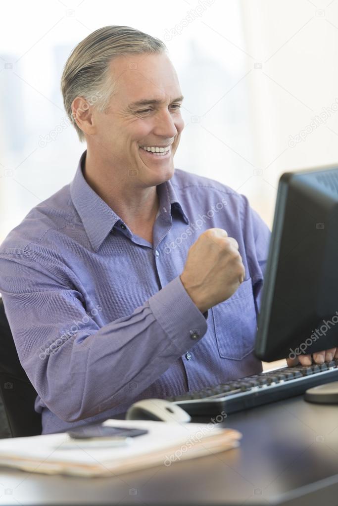 Businessman With Clenched Fist Looking At Computer In Office