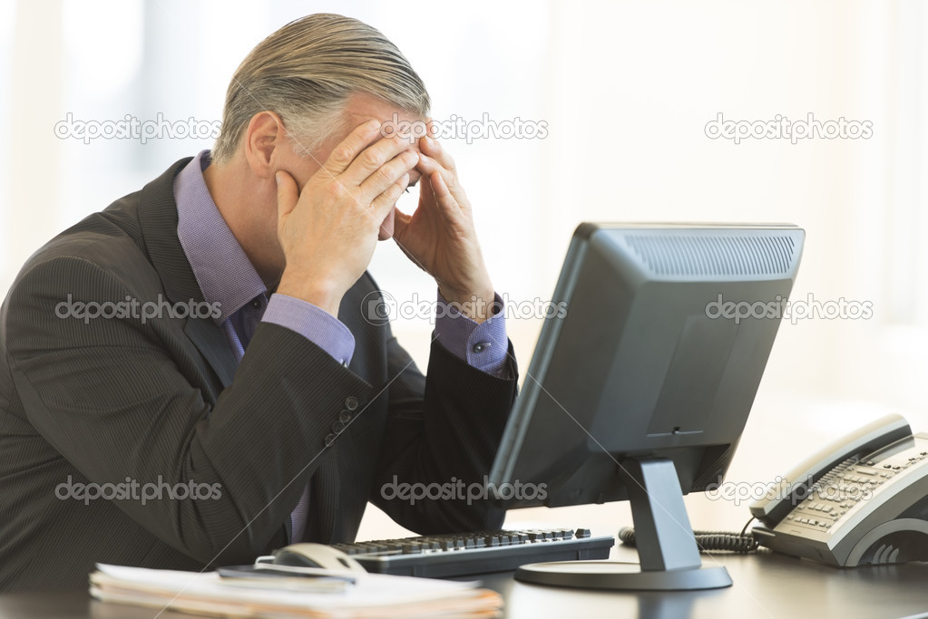 Businessman With Head In Hands Sitting At Desk