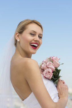 Cheerful Bride With Flower Bouquet Against Clear Blue Sky clipart