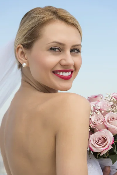 Braut im rückenlosen Kleid mit Blumenstrauß vor klarem Himmel — Stockfoto