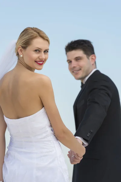 Vackra brud Holding brudgummens händer mot klarblå himmel — Stockfoto