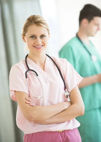 Doctor Standing Arms Crossed With Colleague In Background At Cli — Stock Photo, Image