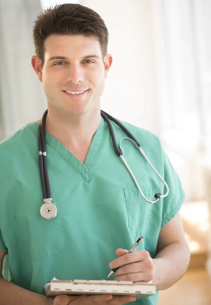 Macho doctor celebración pluma y portapapeles en clínica — Foto de Stock