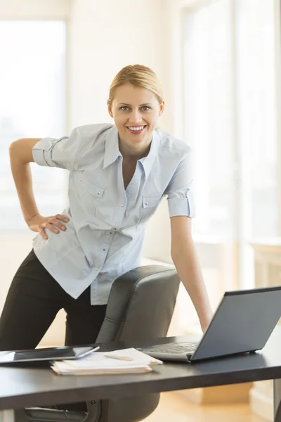 Geschäftsfrau mit Hand auf Hüfte am Schreibtisch — Stockfoto