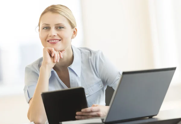 Деловая женщина с рукой на подбородке держит цифровой планшет в офисе — стоковое фото
