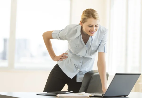 Geschäftsfrau mit der Hand an der Hüfte blickt im Büro auf Laptop — Stockfoto