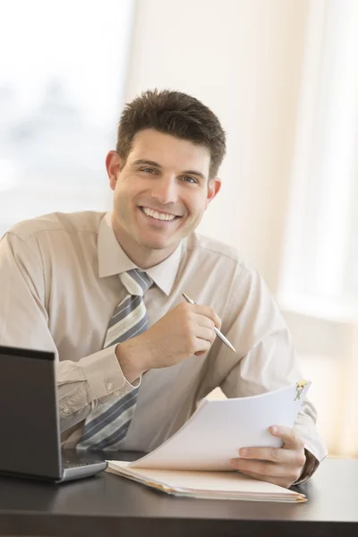 Empresario con documentos y pluma sentado en el escritorio Fotos de stock