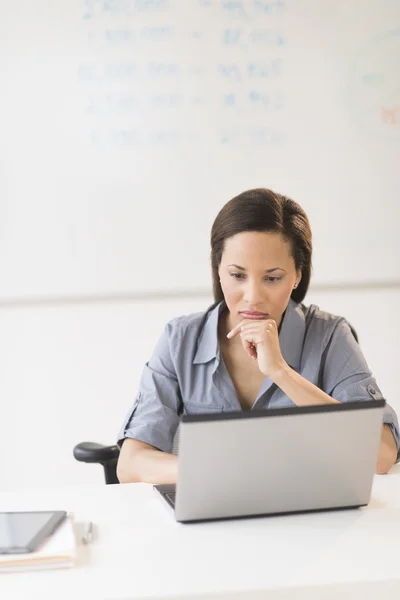 Kobieta z ręki na brodzie korzysta z laptopa w biurze — Zdjęcie stockowe