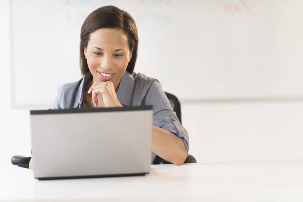 Affärskvinna med hand på hakan med laptop på skrivbordet — Stockfoto