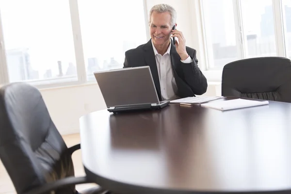 Geschäftsmann benutzt Handy beim Blick auf Laptop — Stockfoto