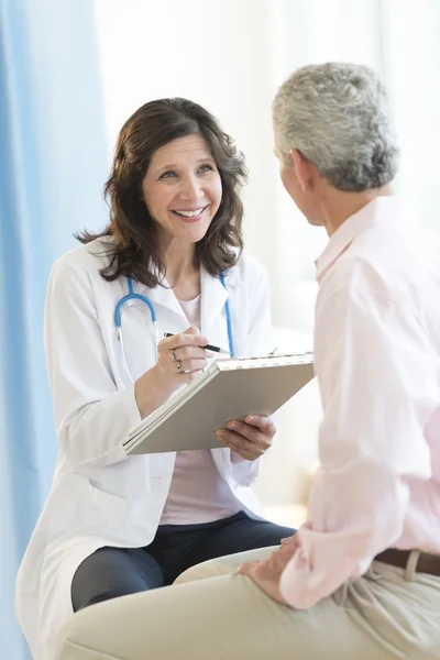 Docteur heureux avec presse-papiers regardant le patient — Photo