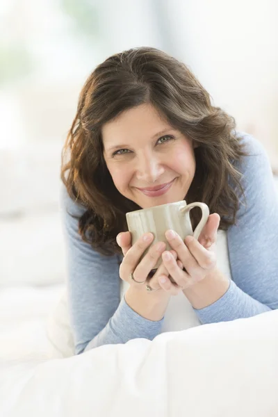 Hermosa mujer sosteniendo taza de café mientras se relaja en la cama — Foto de Stock