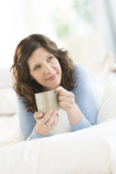 Nachdenkliche Frau mit Kaffeebecher im Bett — Stockfoto