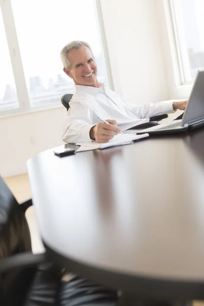 Businessman Smiling While Writing On Document At Desk Royalty Free Stock Photos