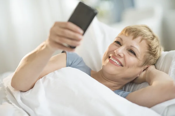 Kadın yatakta yatan iken cep telefonunuzu kullanarak — Stok fotoğraf
