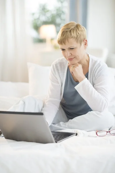 Kvinna med laptop på säng hemma — Stockfoto