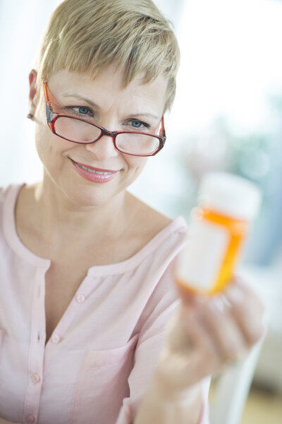 Женщина смотрит на бутылку с таблетками
