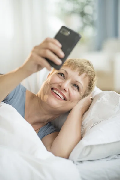 Fröhliche Frau mit Smartphone im Bett — Stockfoto
